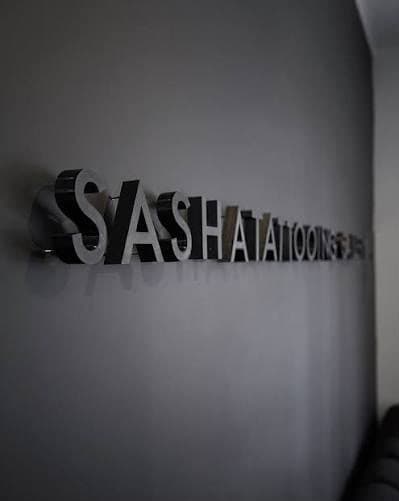 The Sashatattooing name in metal letters on a dark studio wall