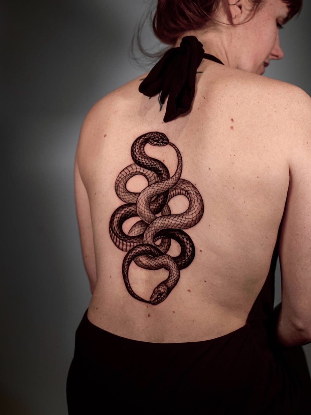Blackwork knotted snakes running down a client's back