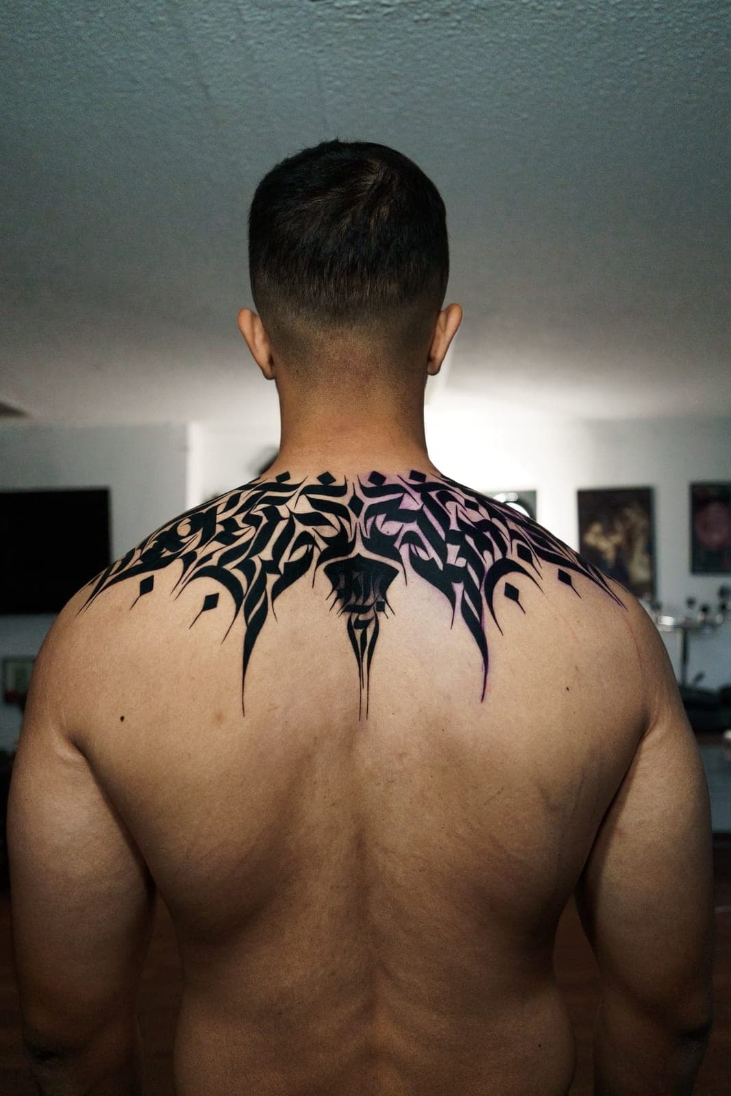 Calligraphy tattoo spreading across a client's shoulders and upper back