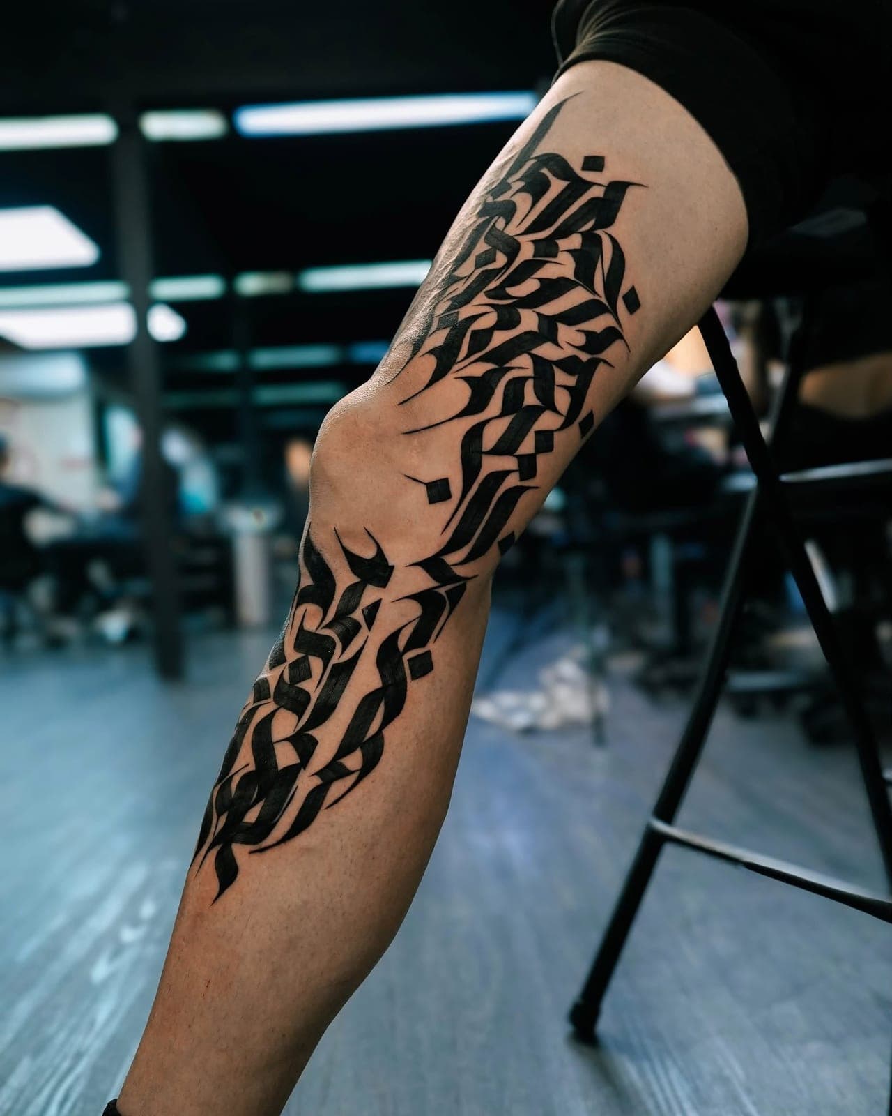 Black calligraphy tattoo running from thigh to calf